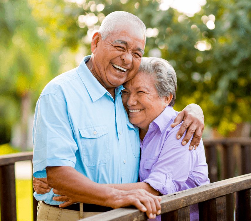 An elderly couple hugging outside